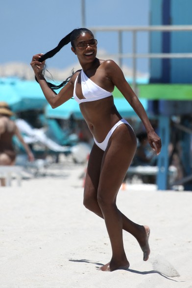 Gabrielle Union in a white bikini on the beach holding her ponytail